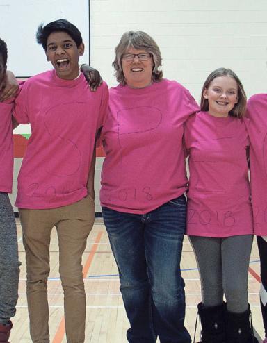 Six adolescents et adolescentes et une femme d'âge moyen, se tenant debout les bras les uns autour des autres, sourient vers l'objectif. Tous et toutes portent des t-shirts roses. Visibilité masquée.