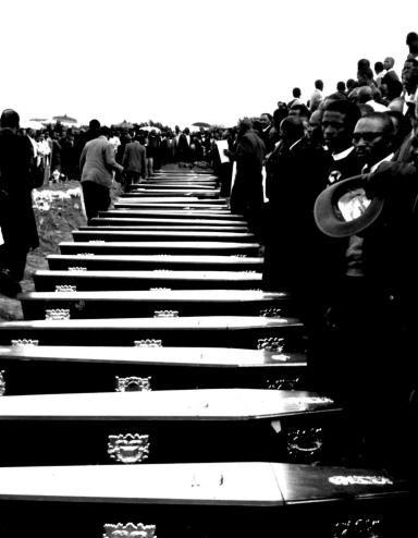 Des gens se tiennent devant une rangée de cercueils. Visibilité masquée.