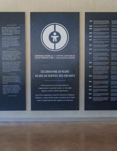 Grands panneaux bleu foncé avec texte et graphiques blancs exposés dans le Corridor communautaire du Musée canadien pour les droits de la personne. Le panneau central comporte un logo circulaire et commémore le 40e anniversaire du Centre canadien de protection de l'enfance. Les deux panneaux de chaque côté présentent du texte bilingue en anglais et en français. Visibilité masquée.