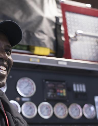 Un homme souriant devant un camion d’incendie. Visibilité masquée.