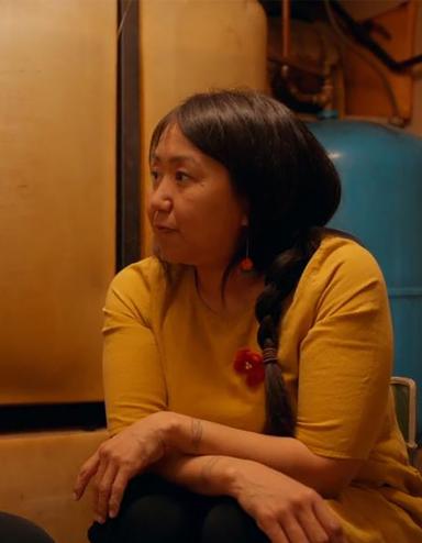 Deux femmes inuites sont assises dans une pièce sombre, l’une en face de l’autre, et discutent de manière intime. L'une porte un chandail rouge, l'autre un chandail jaune. Visibilité masquée.