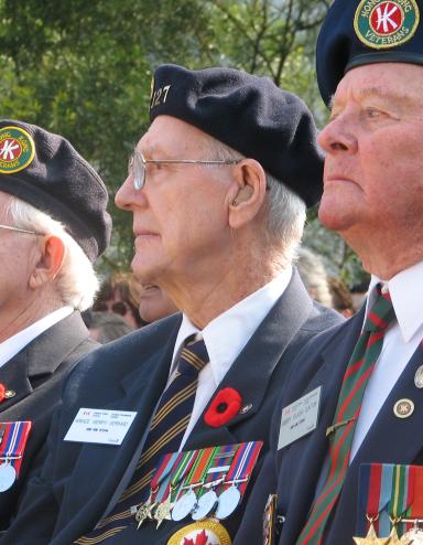 Trois hommes âgés, membres de la Légion canadienne, sont assis côte à côte. Tous les trois portent le coquelicot du jour du Souvenir sur leur uniforme.
