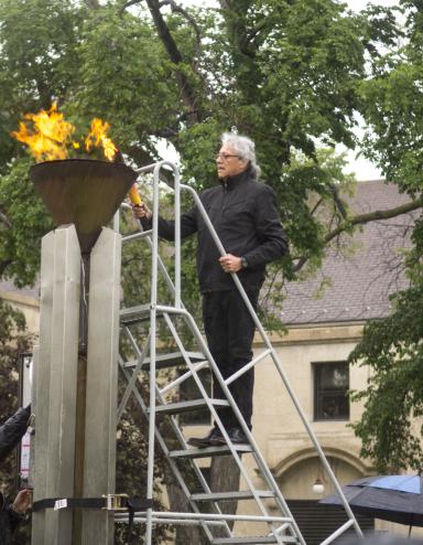 Un homme tenant un flambeau est debout sur une échelle pour allumer une flamme dans une vasque en cuivre.