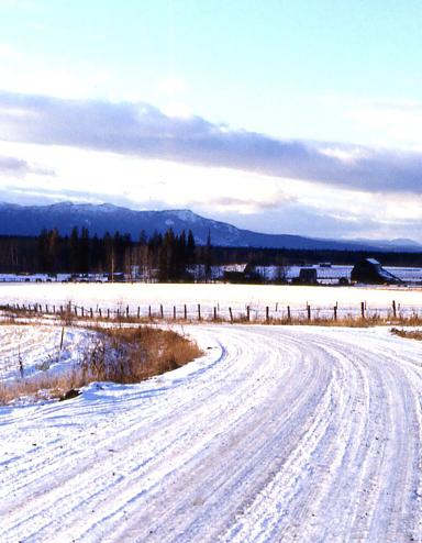 Une route de campagne couverte de neige; on voit des montages au loin.