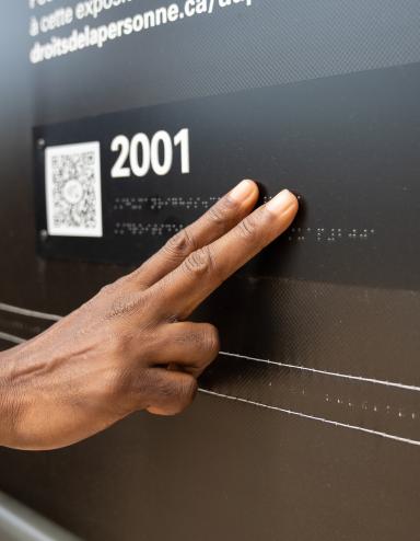 Une main touche des lettres en braille dans une exposition muséale.