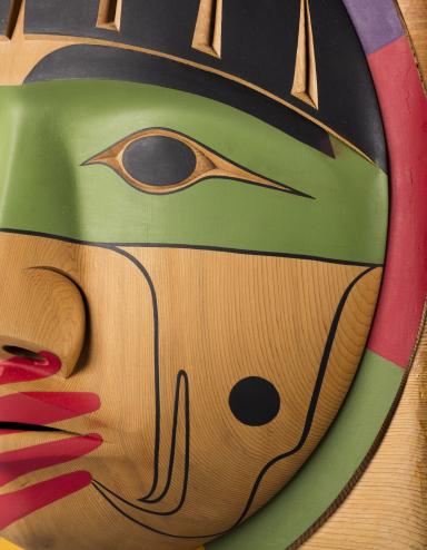 Un plan rapproché d’une boîte en bois, sur laquelle est sculpté un visage dont la bouche est recouverte d’une main peinte en rouge.