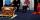 Deux hommes et une femme assis devant un arrière-plan blanc décoré de flammes stylisées. À leur droite, on voit une bannière verticale sur laquelle on peut lire « Truth & Reconciliation Commission of Canada ». et devant eux se trouve une boîte rectangulaire en bois sculpté. Sur le côté qui fait face à l'objectif, on voit un visage rond qui pleure.