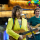 Deux guitaristes en tenues vives et colorées chantent dans des microphones devant une arche de ballons.