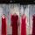 Six robes rouges sont suspendues à des cintres devant une toile de fond. Cette toile de fond montre l’image d’une forêt de bouleaux dans laquelle d’autres robes rouges sont suspendues.