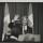 Une photographie en noir et blanc de Nelson Mandela debout derrière un podium. Il sourit et fait signe de la main.
