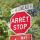 Un panneau d’arrêt et un panneau de signalisation de rue, en français et en anglais, se trouvent devant des arbres.