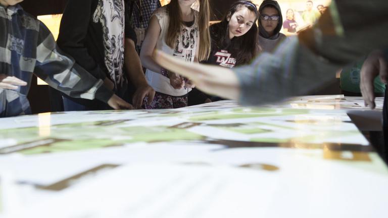 Un groupe d'élèves regardent la surface lumineuse d'une table interactive. Visibilité masquée.