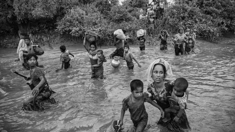 Un groupe de femmes et d’enfants rohingyas marchent dans un canal où l’eau est de deux à trois pieds de profondeur, en transportant leurs effets personnels.