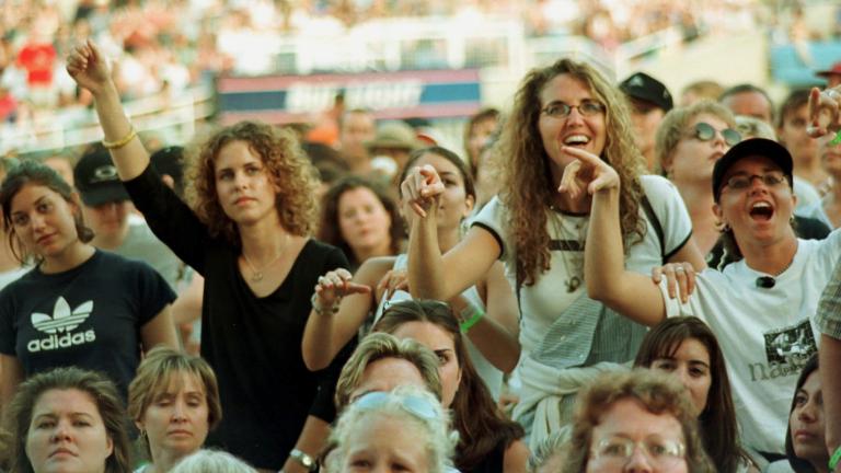 Une foule de femmes, regardant un spectacle hors champ. Un bon nombre d’entre elles sourient, et certaines ont les bras levés. On peut voir une foule plus nombreuse assise dans un stade derrière elles.