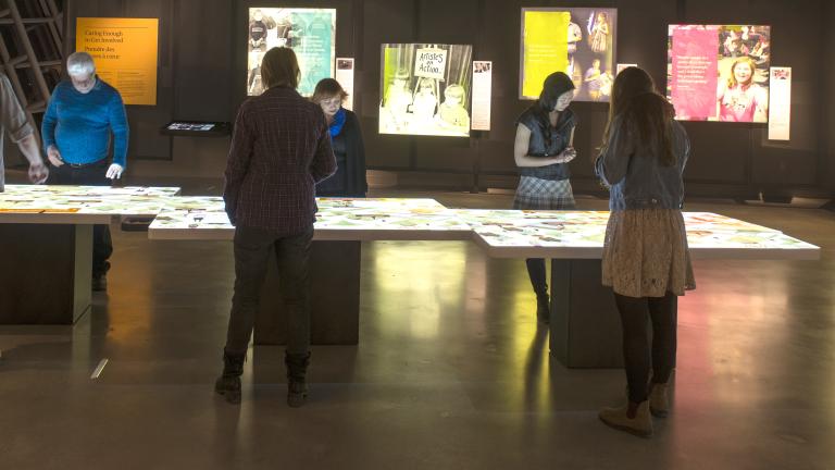 Six personnes observent une table lumineuse. Des images rétro-éclairées en couleur sont sur le mur.