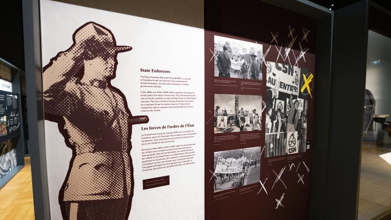 Panneau d'exposition avec une image d'un agent de la GRC au garde-à-vous et un texte indiquant « Les forces de l'ordre de l'État ». Visibilité masquée.