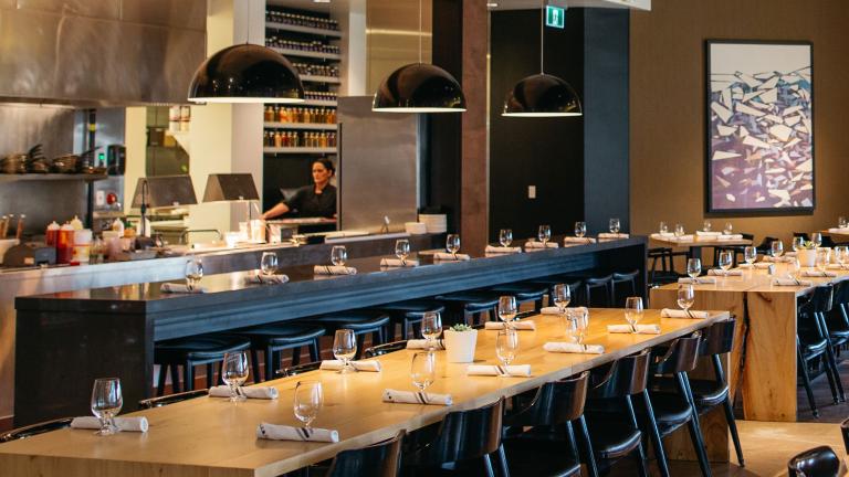 La salle à manger d'un restaurant avec de longues tables et un aperçu de la cuisine. Visibilité masquée.