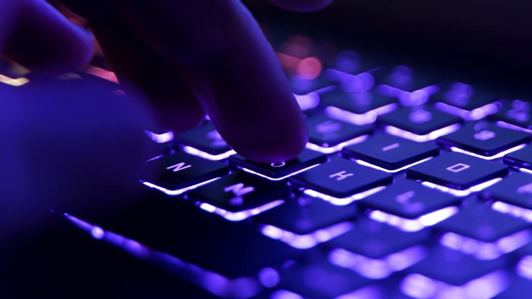 Une main plane au-dessus d’un clavier d’ordinateur, prête à appuyer sur une touche. Visibilité masquée.