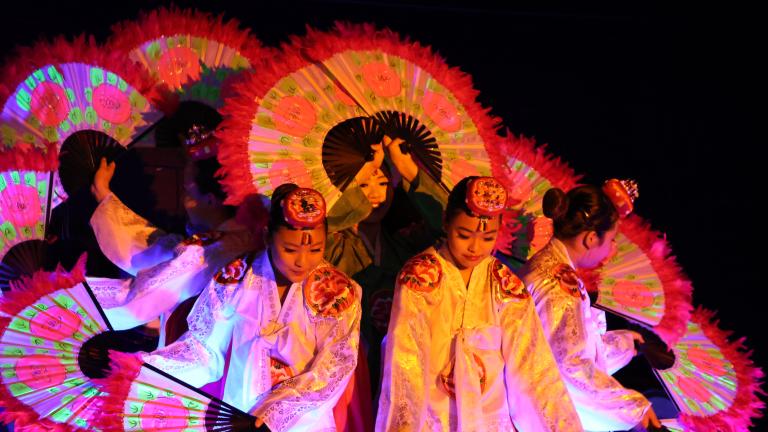 Des danseuses coréennes tenant de grands éventails ornés de fleurs sont regroupées de façon que leurs éventails forment un cercle.