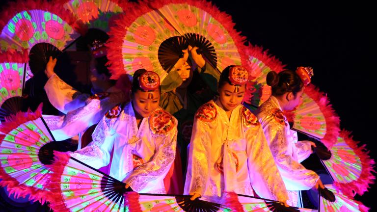 Des danseuses coréennes tenant de grands éventails ornés de fleurs sont regroupées de façon que leurs éventails forment un cercle. Visibilité masquée.