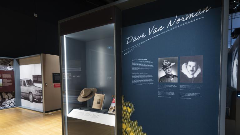 Une vitrine contenant un chapeau Stetson et des magazines se trouve à gauche d’un panneau d’exposition avec des photographies, du texte et les mots « Dave Van Norman ».
