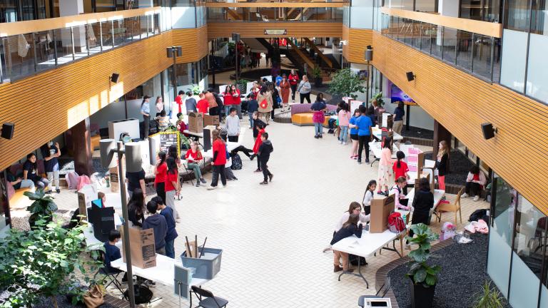 De nombreuses personnes sont rassemblées dans un espace intérieur ouvert où sont disposées des tables et des affiches. Visibilité masquée.