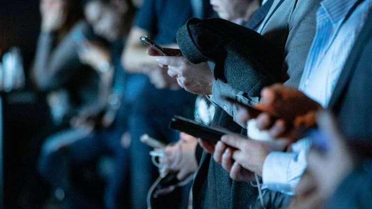 Un groupe de personnes utilisant leurs téléphones portables debout. Visibilité masquée.