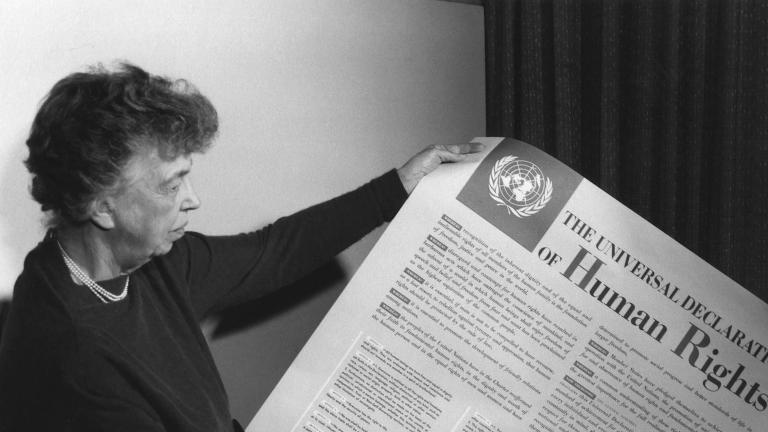 Une personne tient une grande feuille de papier recouverte de texte et dont le gros titre est « The Universal Declaration of Human Rights. » Visibilité masquée.