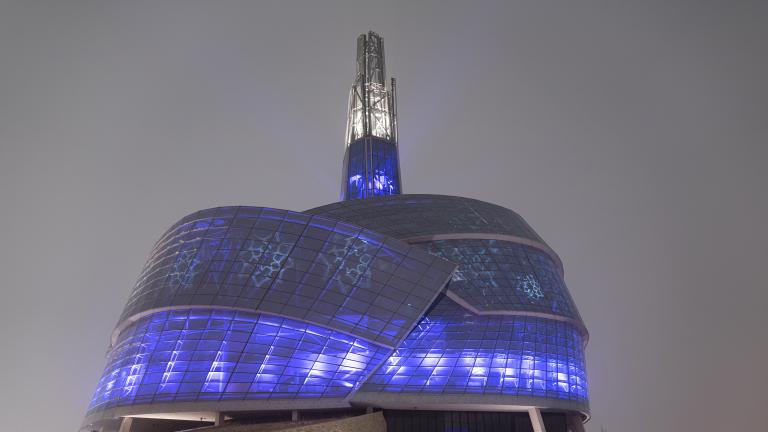  Un édifice recouvert de panneaux de verre illuminé de bleu et de violet. Des motifs de flocons de neige sont également projetés sur les fenêtres. Visibilité masquée.