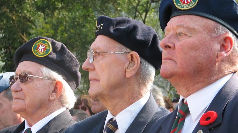 Trois hommes âgés, membres de la Légion canadienne, sont assis côte à côte. Tous les trois portent le coquelicot du jour du Souvenir sur leur uniforme. Visibilité masquée.