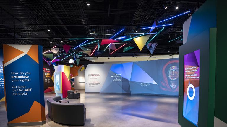 Une galerie de musée où on voit des oeuvres d'art projetées sur de grands écrans et formes géométriques colorées. Visibilité masquée.