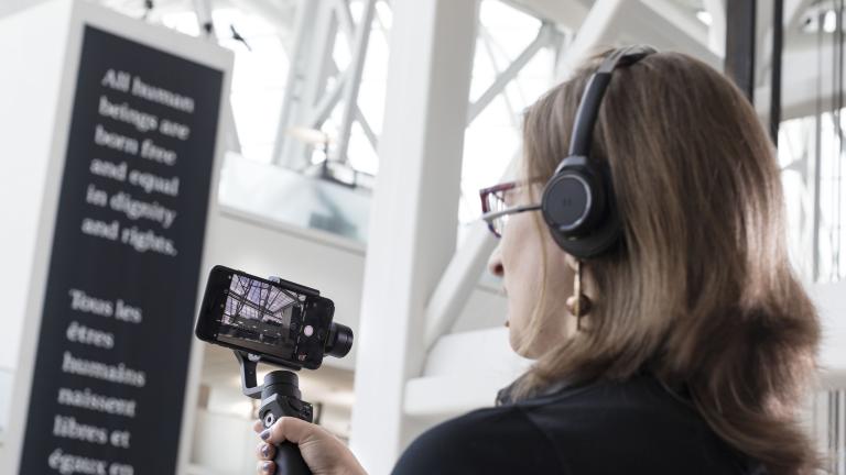 Une femme tient une barre avec un téléphone portable fixé au bout et utilise l'écran pour regarder quelque chose hors champ. Visibilité masquée.