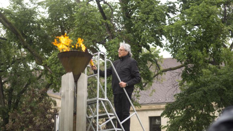 Un homme tenant un flambeau est debout sur une échelle pour allumer une flamme dans une vasque en cuivre. Visibilité masquée.