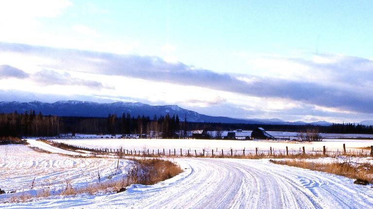Une route de campagne couverte de neige; on voit des montages au loin. Visibilité masquée.