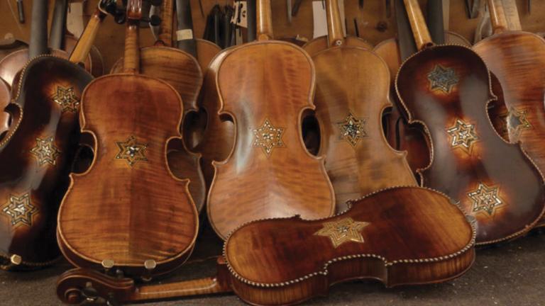 Plusieurs violons restaurés sont présentés appuyés les uns sur les autres dans une pile. Chacun des violons porte au moins une étoile de David. Visibilité masquée.