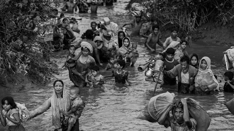 Des femmes, des enfants et des hommes rohingyas marchent dans l’eau d’une rivière qui leur monte jusqu’à la taille. Certaines personnes portent des jeunes enfants alors que d’autres portent des sacs de possessions, dont des articles ménagers. Visibilité masquée.
