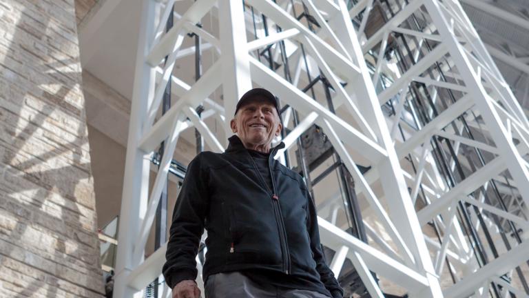 Antoine Predock, l'architecte du Musée, pris en photo en contre-plongée à l’intérieur du Musée. Des poutres blanches s’étendent vers le haut derrière lui.