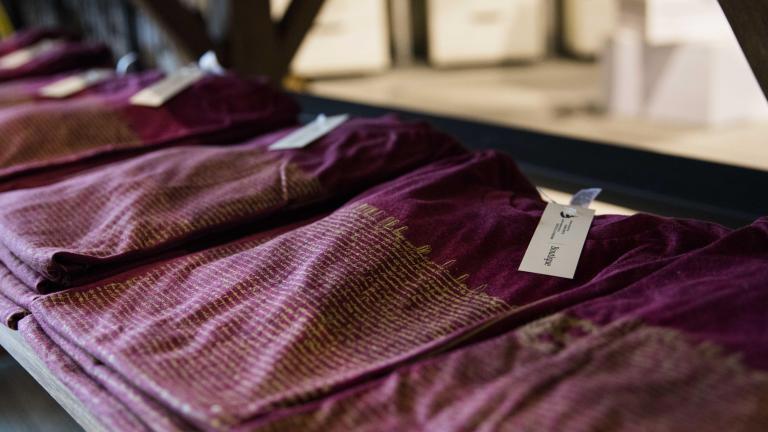 Des piles de trois ou quatre t-shirts couleur rouge vin pliés sont posées sur une table en bois. Visibilité masquée.