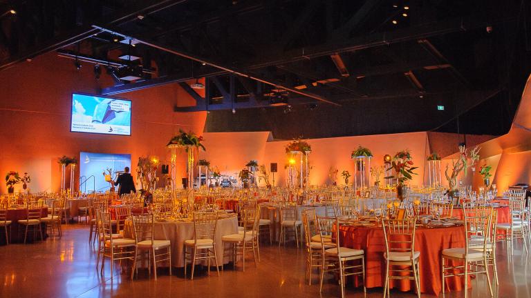 Une grande salle avec de hauts plafonds, remplie de tables rondes avec des couverts formels. 