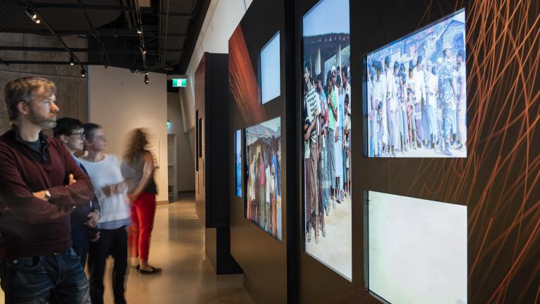 Quelques personnes regardent une élément d'exposition comprenant des photographies numériques en couleur.