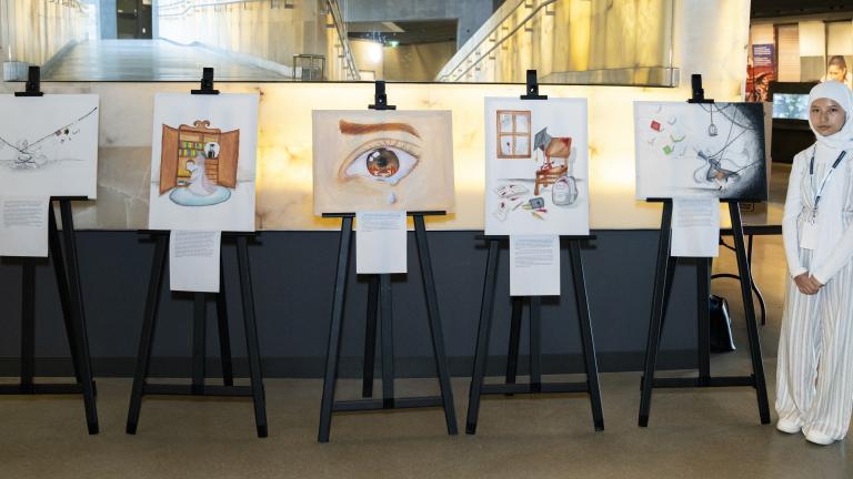 Une élève se tient debout à côté de cinq chevalets sur lesquels sont exposées ses œuvres originales.