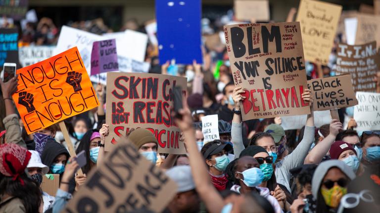 Un grand groupe de personnes tenant des pancartes avec des slogans en anglais qui disent, entre autres, « Les vies noires comptent », « Assez, c’est assez » et « Votre silence est une trahison ». Visibilité masquée.