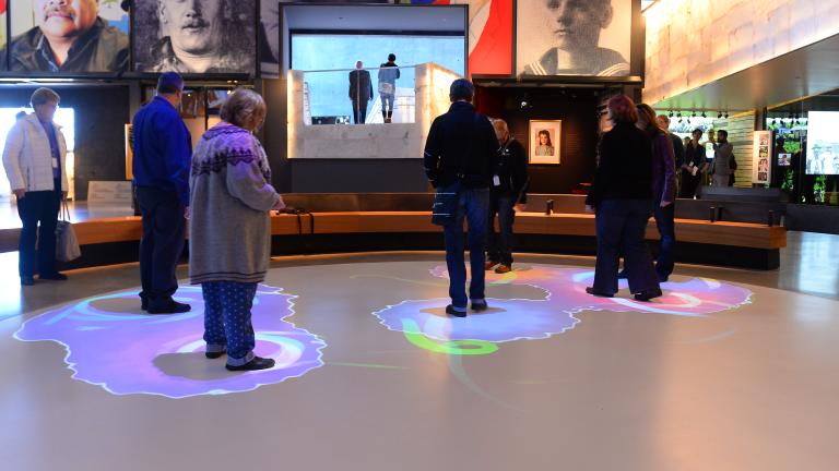 Un groupe de personnes se tient dans une partie d'un cercle blanc. Des lumières bleues et violettes sont projetées sur le sol autour de chaque personne. Visibilité masquée.