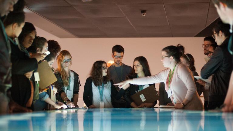 Un groupe de jeunes debout autour d’une table dont la surface interactive émet une lumière bleue et blanche. Visibilité masquée.