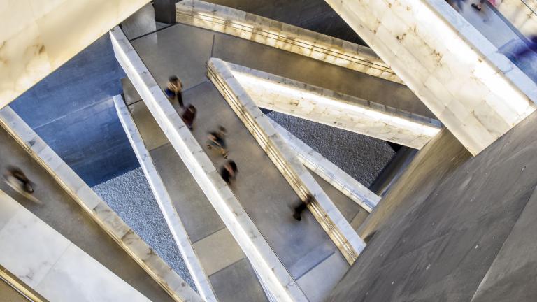 Vue en plongée des rampes en albâtre du Musée qui s’entrecroisent. On voit des gens marcher sur les rampes. Visibilité masquée.