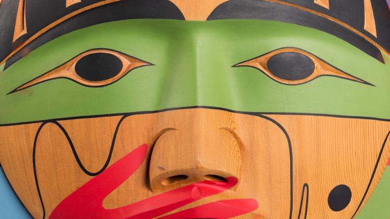 Une boîte en bois, sur laquelle est sculpté un visage dont la bouche est recouverte d’une main peinte en rouge. Visibilité masquée.