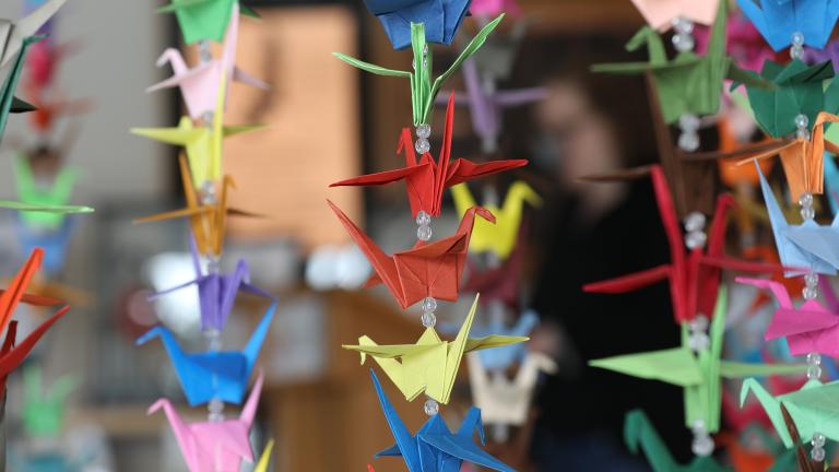 Des grues en papier coloré en origami sont suspendues en rangées verticales. Visibilité masquée.