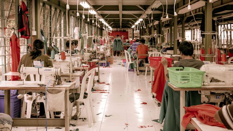 Des travailleuses de l’industrie du vêtement sont assises à des bureaux avec des machines à coudre dans un entrepôt. Visibilité masquée.