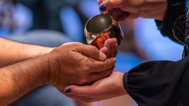 Une personne verse de l’eau d'une tasse en cuivre dans les mains d’une autre personne. Visibilité masquée.