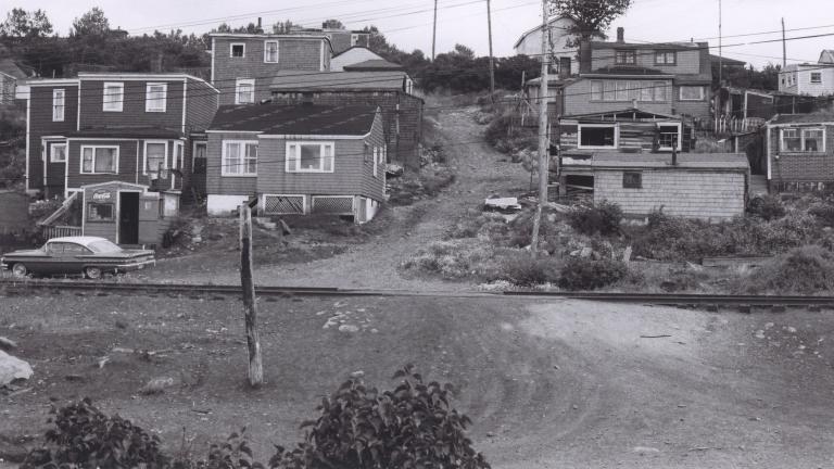 Une image en noir et blanc d’une douzaine de maisons sur une colline. Au milieu de l’image, on voit un chemin de terre qui monte la colline entre les maisons. Visibilité masquée.